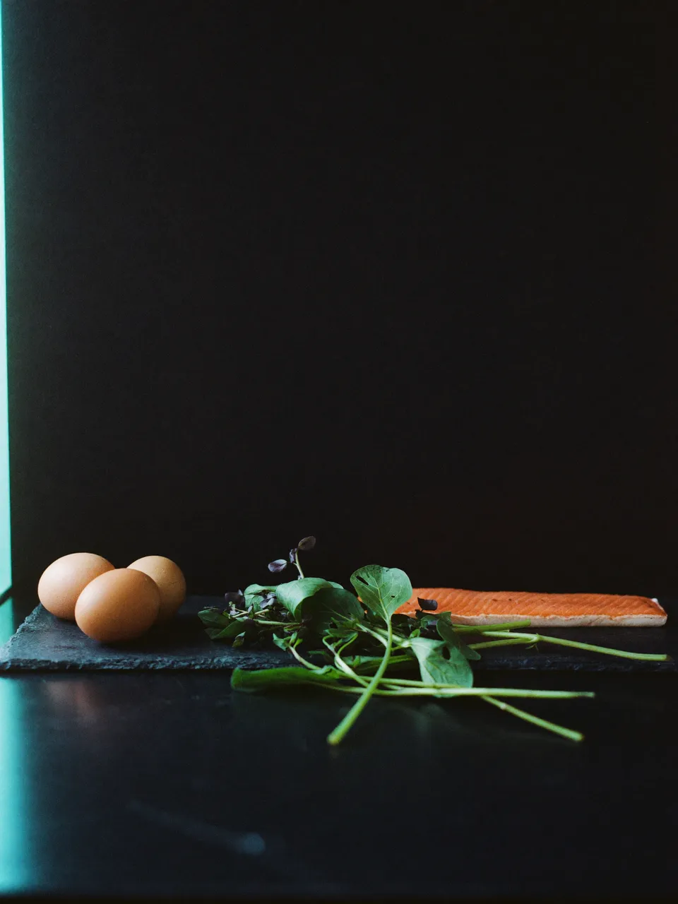 Eier, frisches Grün und Lachs auf dunklem Schiefer